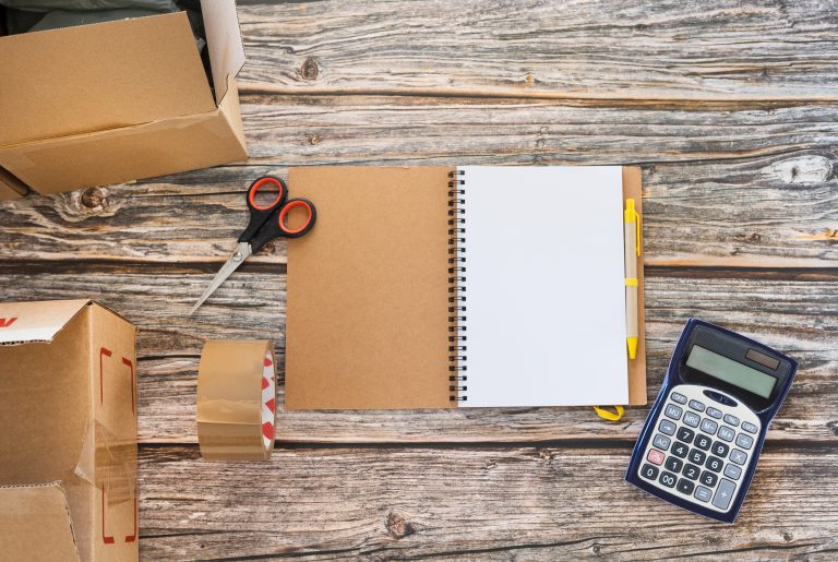 Blank notebook on the table next to cardboard boxes and calculat